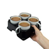 Light grey Muggi tray holding four white mugs with tea or coffee, held in a hand, white background, in use view.