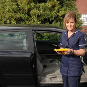 Woman in navy uniform holding yellow folder by open car with Hospital Direct Car Slide Sheet, shown ready for use, side view.