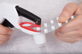 Pivotell Pill Popper pressing a tablet from a blister pack, held by hand, in use close-up.