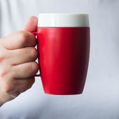 Red ORNAMIN mug with internal cone and white rim, held in a persons hand against a plain white background, in use view.