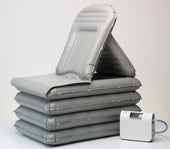 Grey Mangar Camel lifting cushion with raised backrest next to white electric air pump, side view.