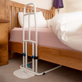 NRS EasyFit Plus+ Bed Rail next to a wooden bed with pink sheets and a white comforter on carpet, side view.