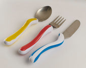 Children’s cutlery set with thick, colourful handles and stainless steel heads on a white surface, top view.