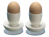 Aidapt white suction egg cups holding brown eggs, each on a small white plate, plain white background, front view.