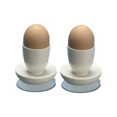 Aidapt white suction egg cups holding brown eggs, each on a small white plate, plain white background, front view.