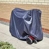 NRS Freestyle Mobility Scooter covered with NRS Storage Cover, parked on pavement next to a brick wall, side view.