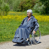 Older woman wearing NRS Freestyle Sleeved Mobility Scooter Poncho outdoors with green plants and yellow flowers, front view.