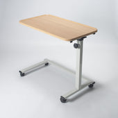 Height adjustable overchair table with light wood top, metal frame and castor wheels, shown from a side angle.