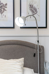 Opera overbed reading lamp next to bed with grey headboard and botanical prints above, side view.