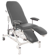 Slate grey treatment chair with adjustable height, armrests, movable leg supports and white frame on casters, front angle.