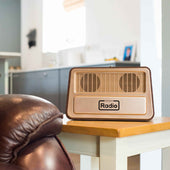Ravencourt One Button Radio on a side table next to a brown leather chair in a bright modern living room, angled view.