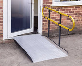 Permaramp-Adjust Ramp with graphite Quickrails positioned at an open doorway of a brick building, shown in use.