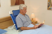Elderly man reading in bed using blue NRS Adjustable Back Support, shown in use.