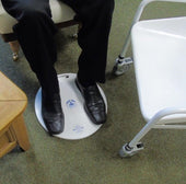 Polymorit MediDisk Turntable in use for transfer between chair and commode, person wearing black shoes on green carpet, side view.
