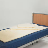 Hospital bed with Thorpe Mill wool bed fleece and two cream pressure pads on top, prevents pressure sores, front angle.