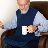 Man sitting in chair wearing burgundy tabard style adult bib, holding a white mug and biscuit, in use front view.
