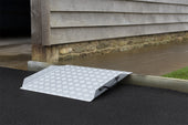 Threshold Lip Ramp with anti-slip surface over a curb by a building, shown in use.