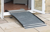 Adjustable ramp bridging a stone patio and an open doorway with tiled flooring, in use view.
