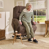 Older woman standing up from a cocoa Motion Healthcare Lawson Four Motor Riser Recliner Chair in a bright living room, in use view.