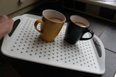 Able2 Stayput Anti-Slip Tray with yellow and black mugs of tea on a dark kitchen counter, in use view.