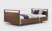 Oak profiling bed with full-length side rails, white bedding, and purple blanket and pillow, side view.