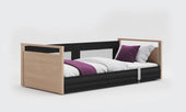 Oak floor bed with wood frame, black sides, white bedding, and a purple accent blanket, front view.