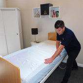 Satin SIBA Sheets by Hospital Direct on a single bed being adjusted by a man, tidy room with shelves, books and teddy bear, in use view.