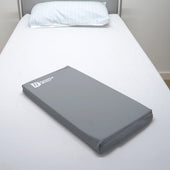 HD Deluxe Limb Pad folding wedge on white bed with striped pillow, designed to relieve pressure, side view.
