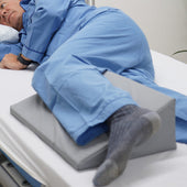 Person in blue pyjamas lying on their side in bed with a Hospital Direct HD Deluxe Limb Pad wedge between their legs, side view.