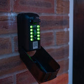 Supra Ark Tamo key safe with illuminated green keys and open compartment, mounted on brick wall, front view.