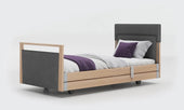 Signature upholstered profiling bed with linen fabric, grey bedding, purple accents and wheels, side view.