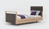 Upholstered profiling bed in linen with wood accents, dark brown panels, white bedding, and a purple throw, front angle view.