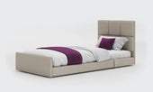 Anthracite profiling floor bed with white bedding, purple throw, and matching pillows, side view.