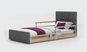 Profiling floor bed in anthracite fabric with side rails and purple bedding on a plain background, front view.