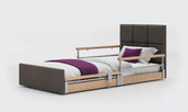 Brown profiling floor bed with side rails, white bedding and a purple blanket, front view.