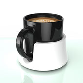Black ceramic mug with latte art on a white anti-spill drink holder and white mug warmer, top view.