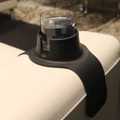 CouchCoaster anti-spill drink holder in grey, holding a glass of water on a white sofa armrest, in use.