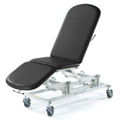 Black SEERS Medical Sterling Electric 3 Section Couch with cushioned sections, electric height adjustment and wheels, side view.