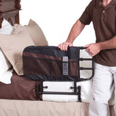 Stander Adjustable Bed Rail with storage pockets fitted to a bed, person holding remote control, in use side view.