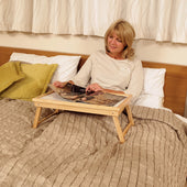 Woman reading on a Homecraft Adjustable Wooden Bed Tray with Legs, using the tray on a bed with bedding and pillows, in use view.