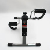 Digital pedal exerciser with resistance dial, foot straps and digital screen, shown from a side angle.