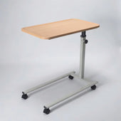 Height adjustable overbed table with light wood top, metal base and four castors, for home use, angled side view.