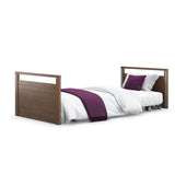 Opera Beds Solo SafeSide Profiling Floor Bed with white blanket, purple throw and two purple pillows on white sheets, front view.