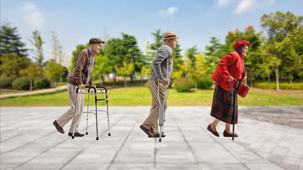 Three elderly individuals using walking aids on a paved path, surrounded by green trees and a clear blue sky.