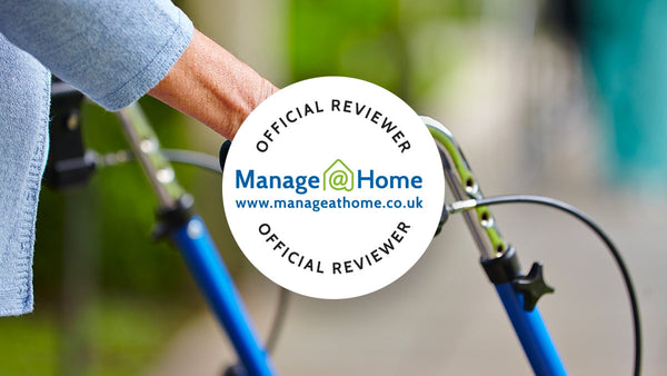 Close-up of hands holding a walker, with a badge saying Official Reviewer and www.manageathome.co.uk. Background: blurry greenery.