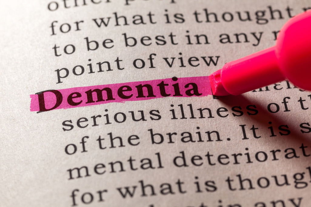 The word Dementia is highlighted in pink on a printed page using a pink highlighter. The surrounding text is blurred and not the focus of the image.