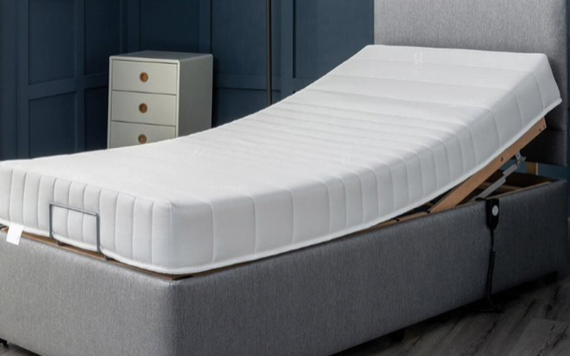 A modern bedroom with an adjustable gray bed frame, small three-drawer bedside cabinet, dark blue walls, and wooden floor.