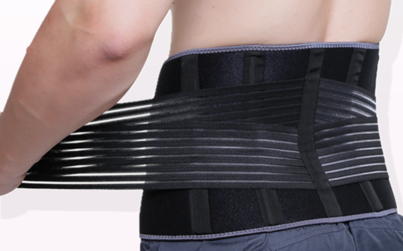 A person wearing a black lumbar support belt around their lower back. The belt is being tightened, showing skin and part of their shorts.