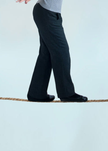 A person in black pants and shoes balances on a tightrope between a rock and an anchor, against a light blue sky. Image