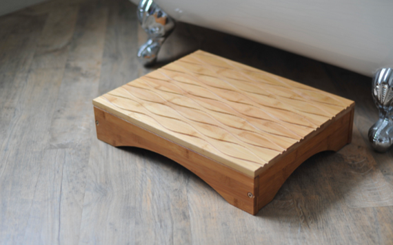 A wooden stool with a diamond pattern sits on the floor near a white bathtub with clawfoot legs.